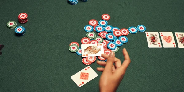 Primo piano di alcune chips di poker già presenti nel piatto, con una giocatrice che valuta se passare o proseguire contro un avversario molto aggressivo.